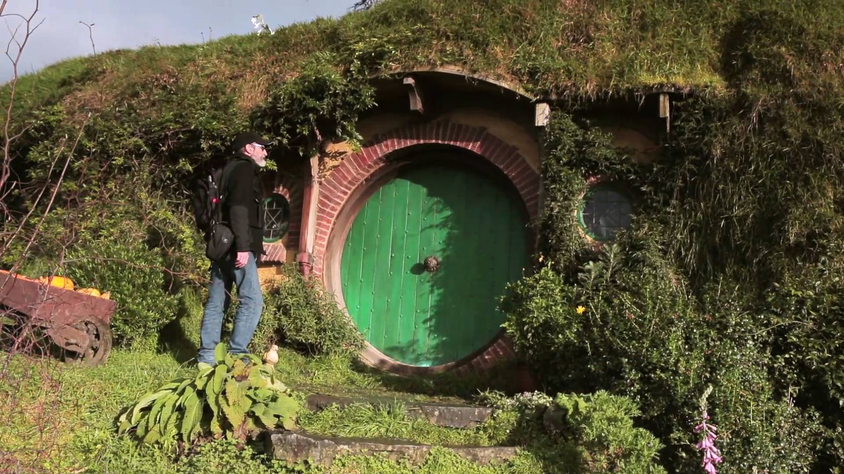 John Howe se tient devant une porte ronde, identique à celle qui mène à la maison de Bilbo dans les films de Peter Jackson.