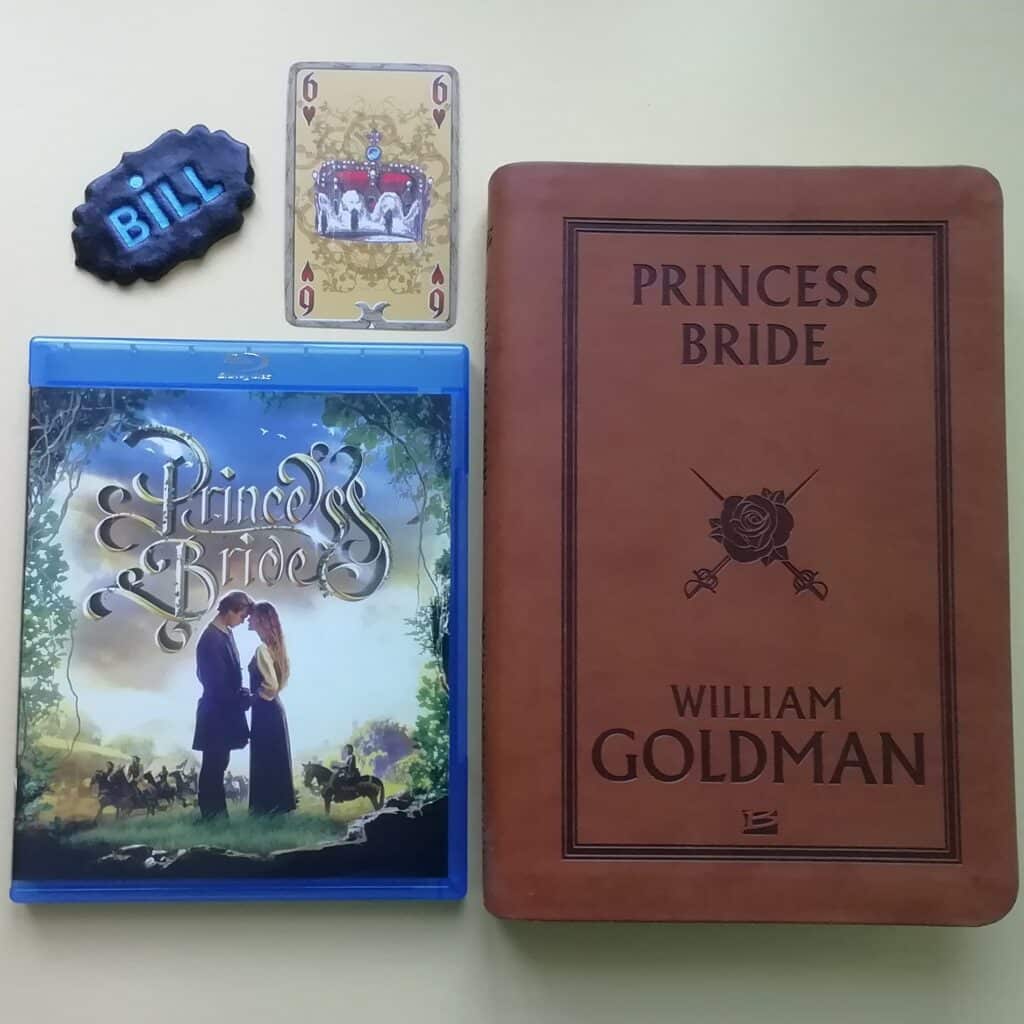 Sur cette photo figurent le roman Princess Bride, le blu-ray du film, une carte qui représente une couronne et le prénom Bill réalité en pâte polymer.