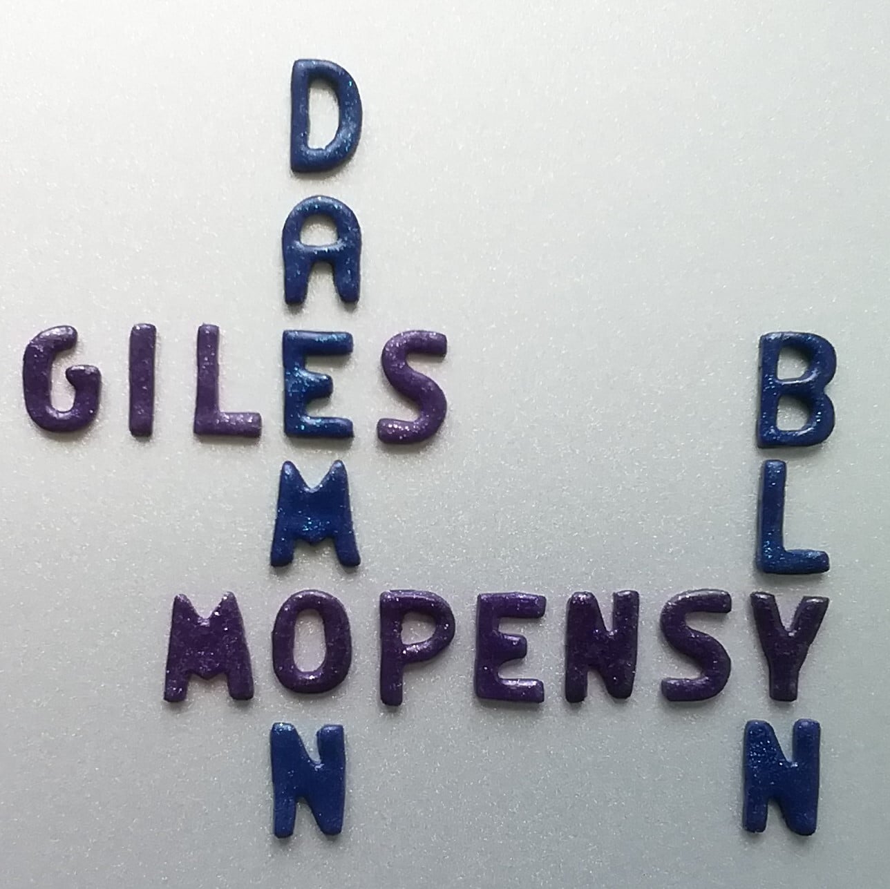 Les mots suivants ont été disposés à la manière du jeu scrabble : Giles, Daemon, Mopensy et Blyn.