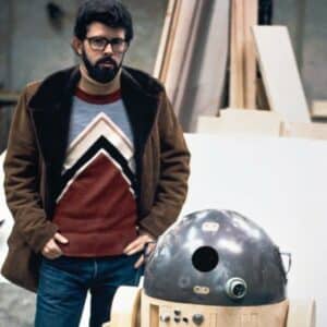 George Lucas se tient près d'un robot qui ressemble à R2D2.